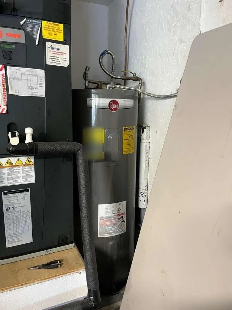 A tank water heater fitted into a utility closet beside the air handler, dielectric unions and shut-off visible