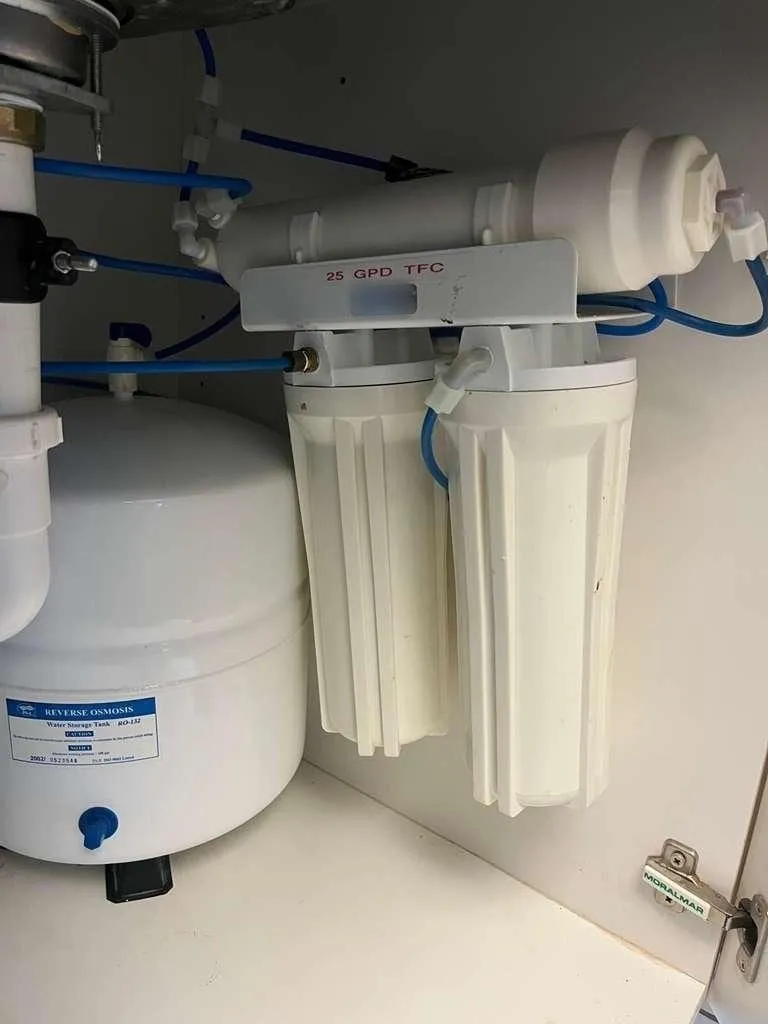 A reverse-osmosis filtration unit and storage tank mounted under a kitchen sink with color-coded quarter-inch lines